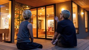 Two people sitting on a wooden deck in front of a building with large glass doors. - Villa Revolla (Makinohara)