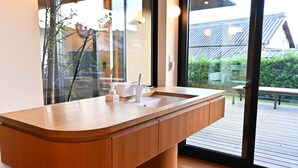 A modern bathroom with a wooden vanity, a white sink, and a large window offering a view of a traditional building and greenery. - Villa Revolla (Makinohara)
