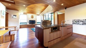 A modern kitchen with wooden cabinetry, a large island with a sink, and a built-in oven. - Villa Revolla (Makinohara)