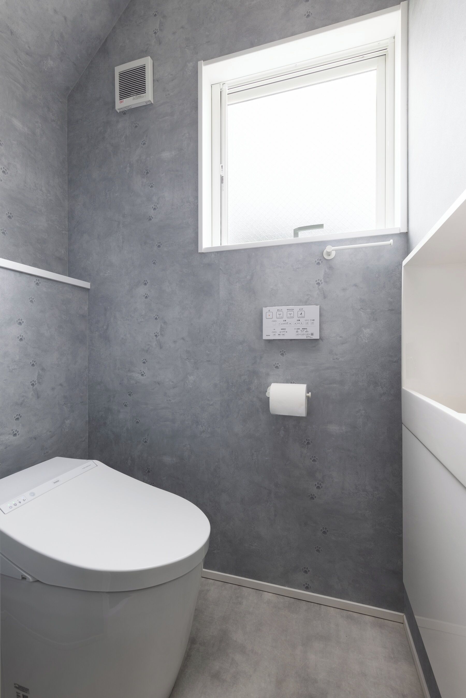 Ein Badezimmer mit Toilette, Fenster, Handtuchhalter und einer fest montierten Bedienkonsole.