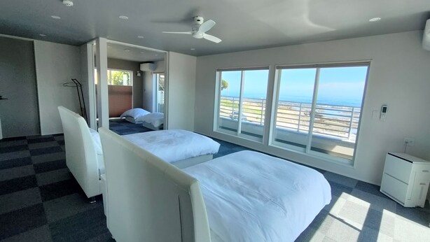A modern hotel room with two beds, a ceiling fan, and a view of the beach. - Bianca (Minamiboso)