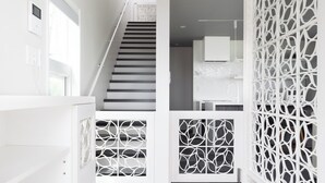 A modern staircase with a geometric railing design, leading to a room with a white cabinet and a television. - Bianca (Minamiboso)