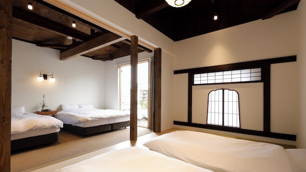 Une chambre avec deux lits, des poutres en bois, une fenêtre à carreaux et un luminaire.