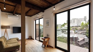 Un salon moderne avec un plancher en bois, un canapé vert, une table d’appoint en bois et une grande fenêtre donnant sur des immeubles.