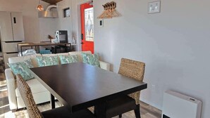 Cozinha moderna com eletrodomésticos brancos, área de jantar com mesa escura e cadeiras brancas, e uma porta vermelha.