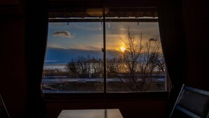 Una habitación con un ventanal grande que da a un estacionamiento y una masa de agua al atardecer.