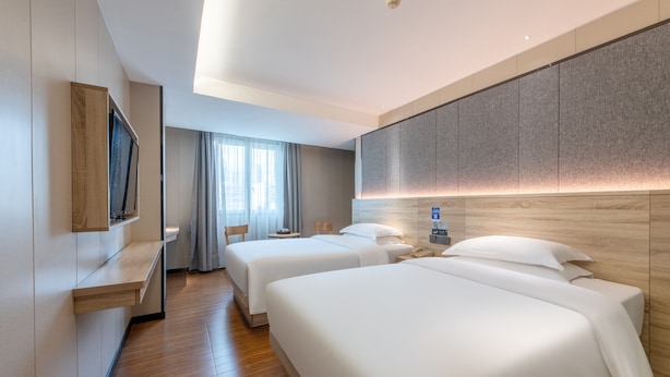 A hotel room with two beds, a TV mounted on the wall, a bedside table, a lamp, and a window with curtains. - Winsome Hotel Guangzhou Tianhe Huajing Road Metro Branch (Guangzhou)
