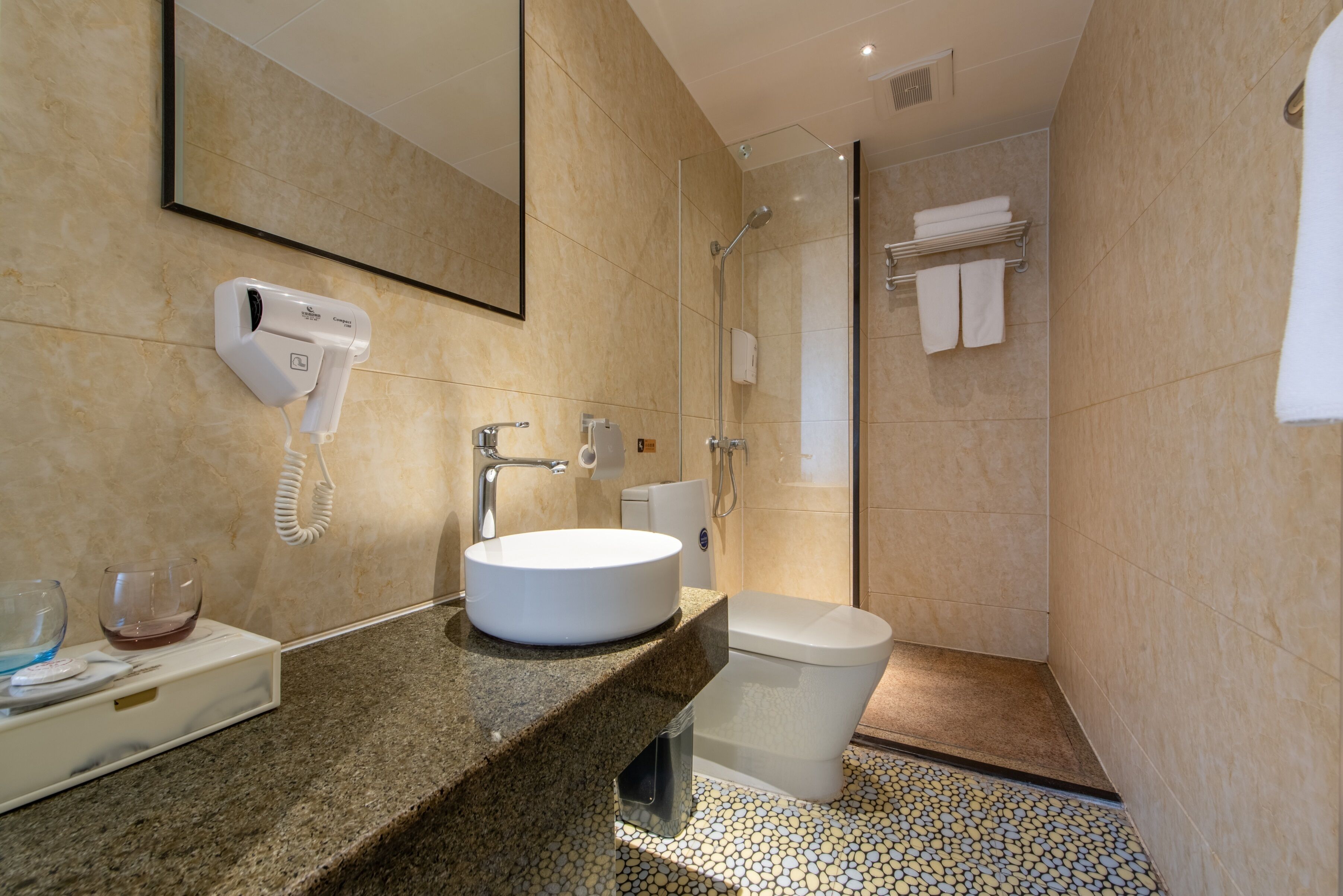 Ein modernes Badezimmer mit Marmorplatte, einem weißen Waschbecken, einem Handhaartrockner und einer Duschkabine aus Glas.
