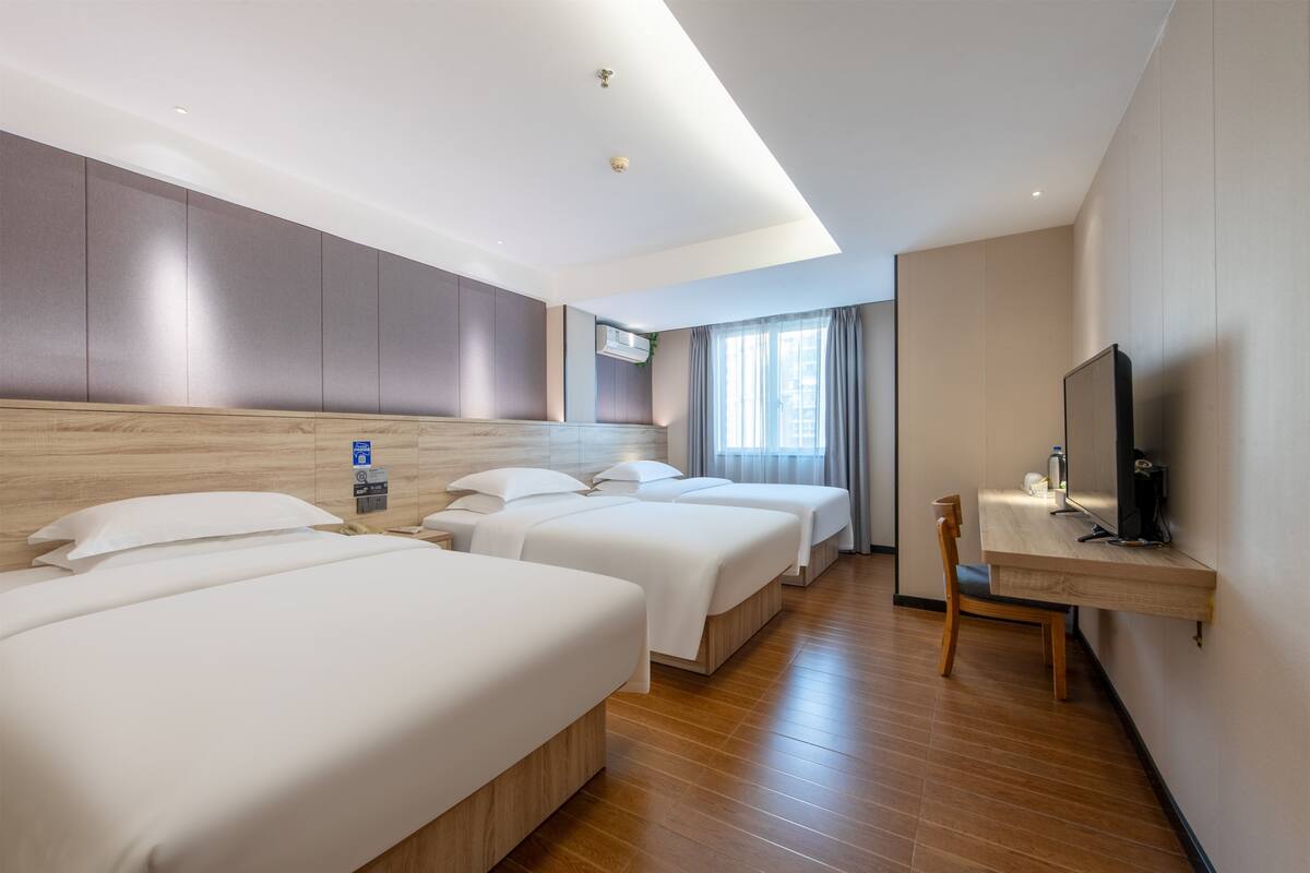 A hotel room with three beds, a desk, a TV, and a window with curtains.