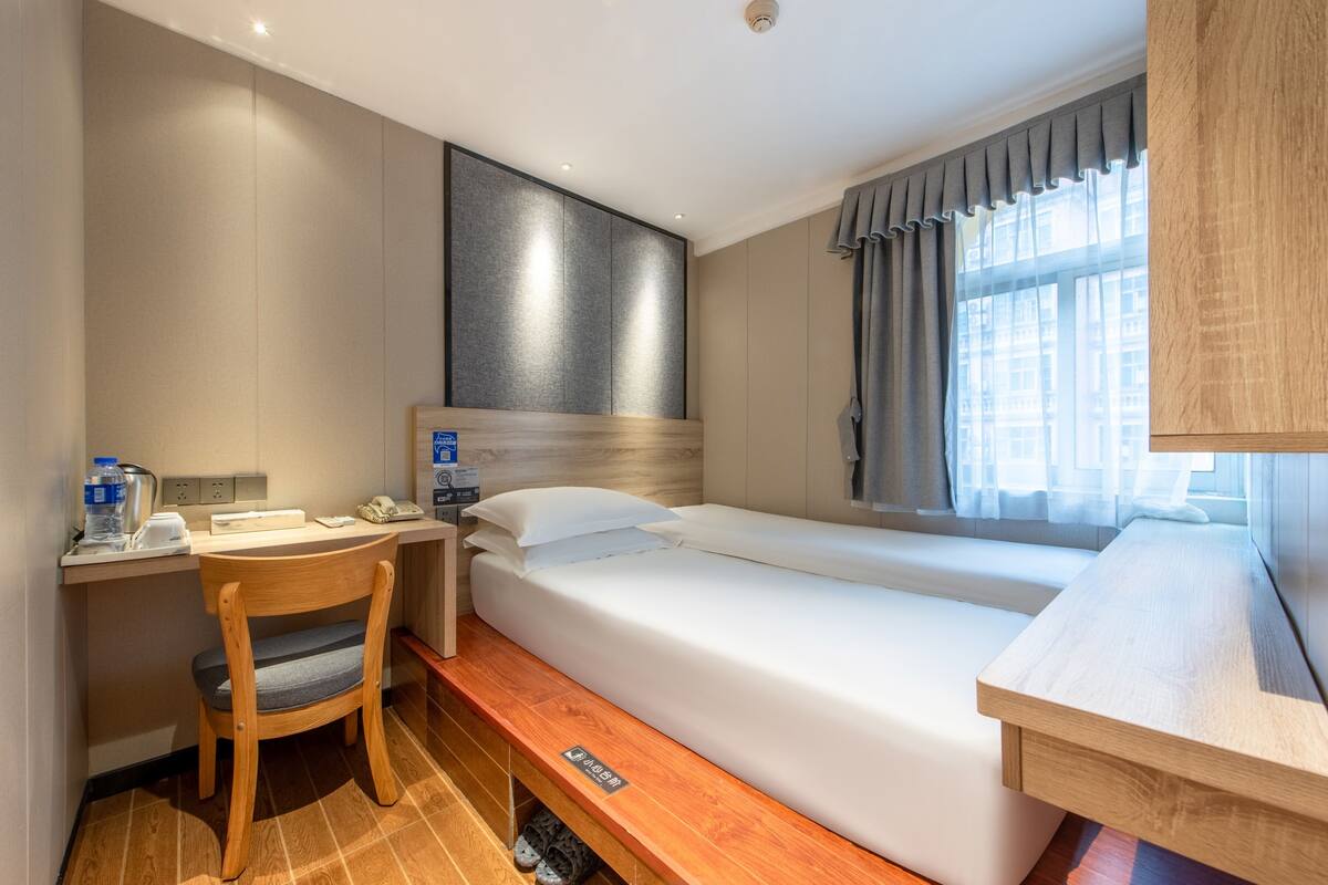 A hotel room with a bed, a desk, a chair, and a window with curtains.