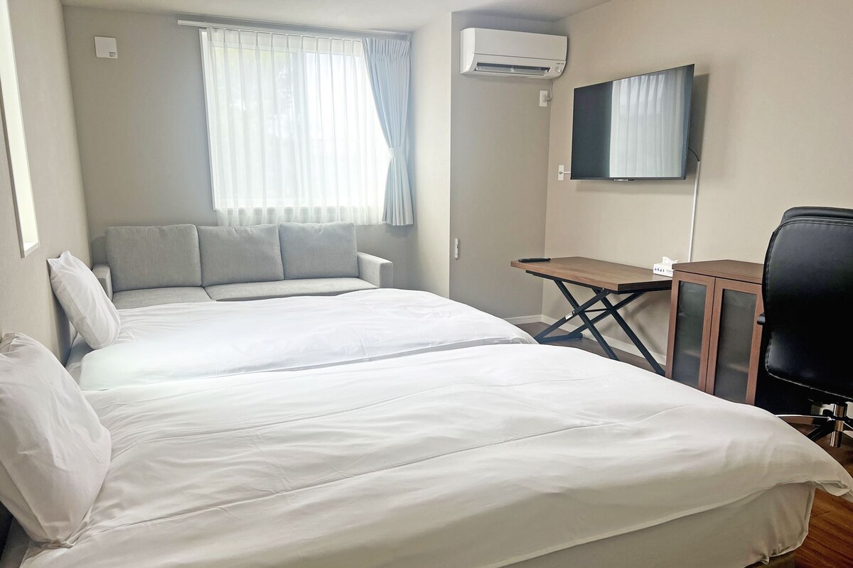 A hotel room with two beds, a desk, a chair, an air conditioner, and a television.