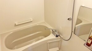 Un baño moderno con una bañera independiente, un cabezal de ducha de mano, un estante pequeño y un espejo.