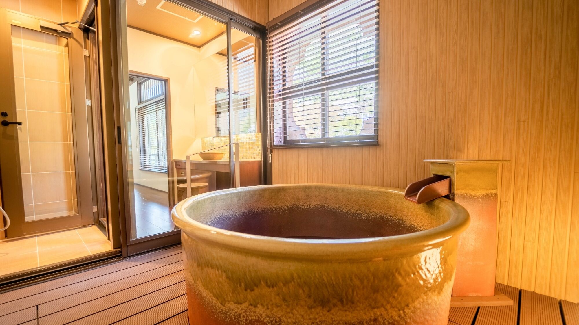 A large ceramic tub in a room with wooden walls and a sliding glass door leading to a bathroom.