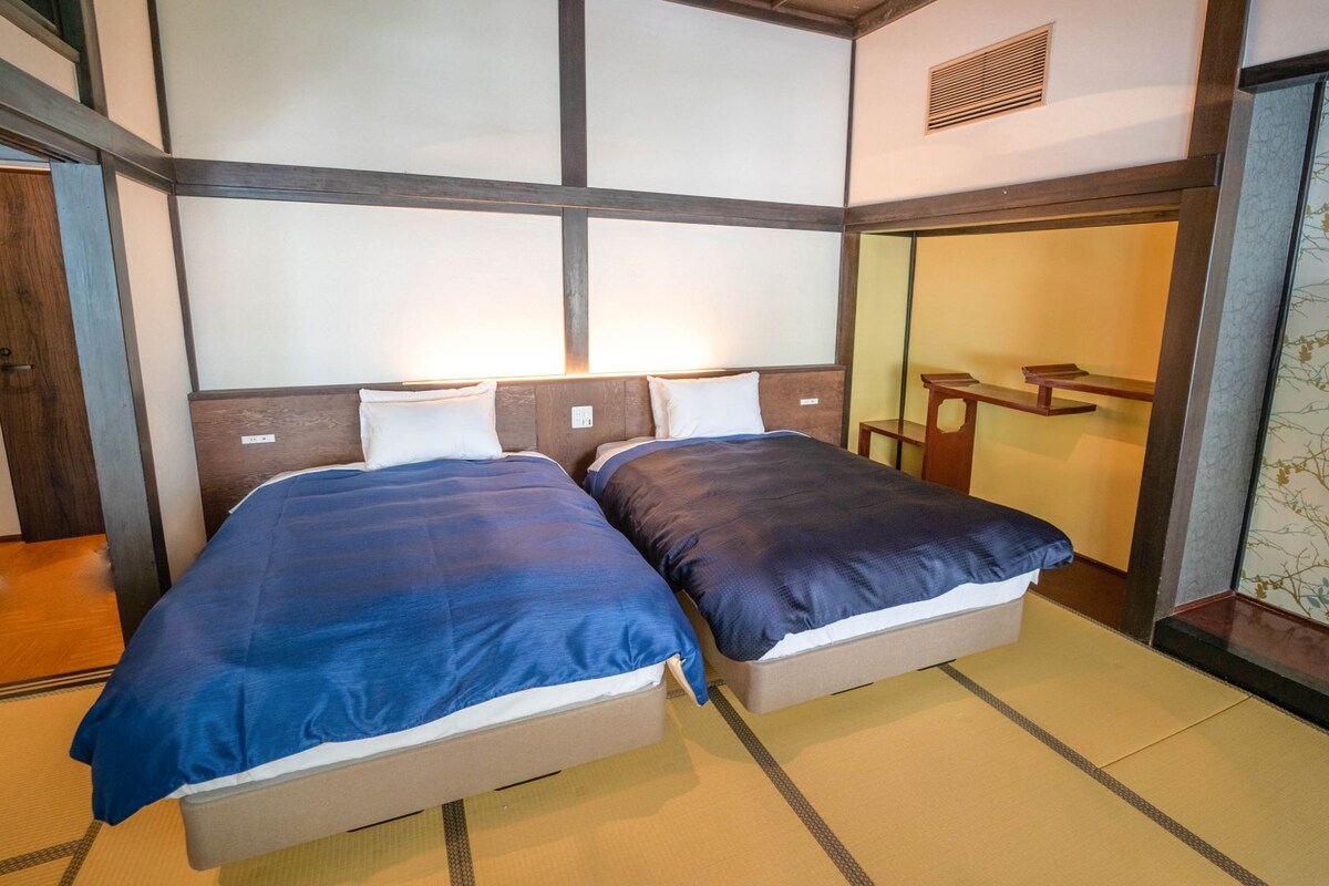 A traditional Japanese-style room with two beds, tatami flooring, and a sliding door leading to a bathroom.