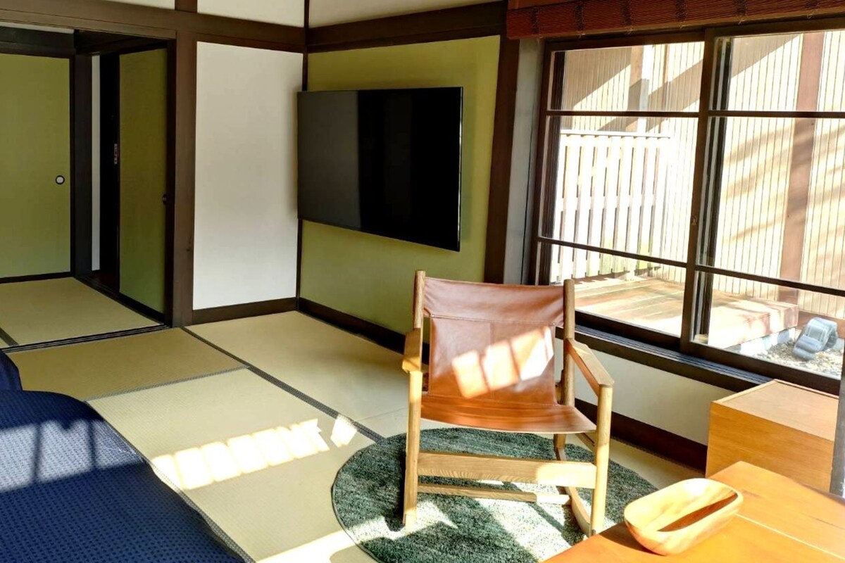A traditional Japanese-style room with tatami flooring, a futon bed, a television, and a view of the outside.