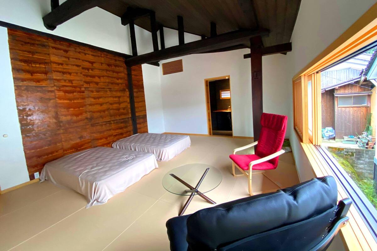 A room with two beds, a red chair, a glass table, and a view of the outside.