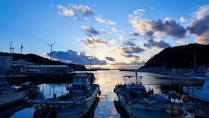 A marina with boats docked, a bridge in the background, and a sunset over the water. - Ryotei Yoshinoya (Matsuura)