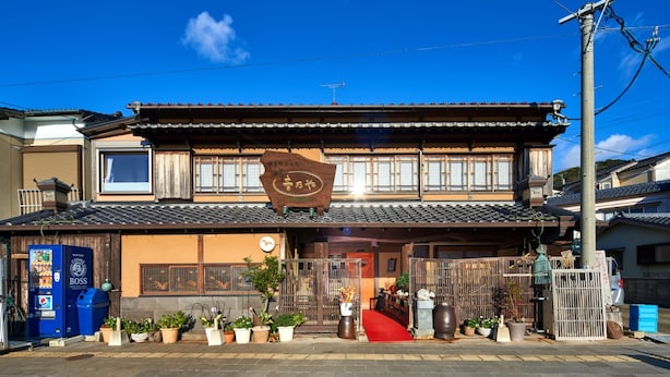 A traditional Japanese building with a signboard, a vending machine, and potted plants in front. - Ryotei Yoshinoya (Matsuura)