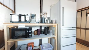 A kitchen with a microwave, coffee maker, and a refrigerator. There are shelves with various containers and a gas canister. - Teihaku Chichibu Nagatoro Folk House Rental (Nagatoro)