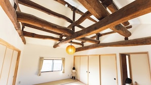 A traditional Japanese room with tatami flooring, wooden beams, sliding doors, and a window with curtains. - Teihaku Chichibu Nagatoro Folk House Rental (Nagatoro)