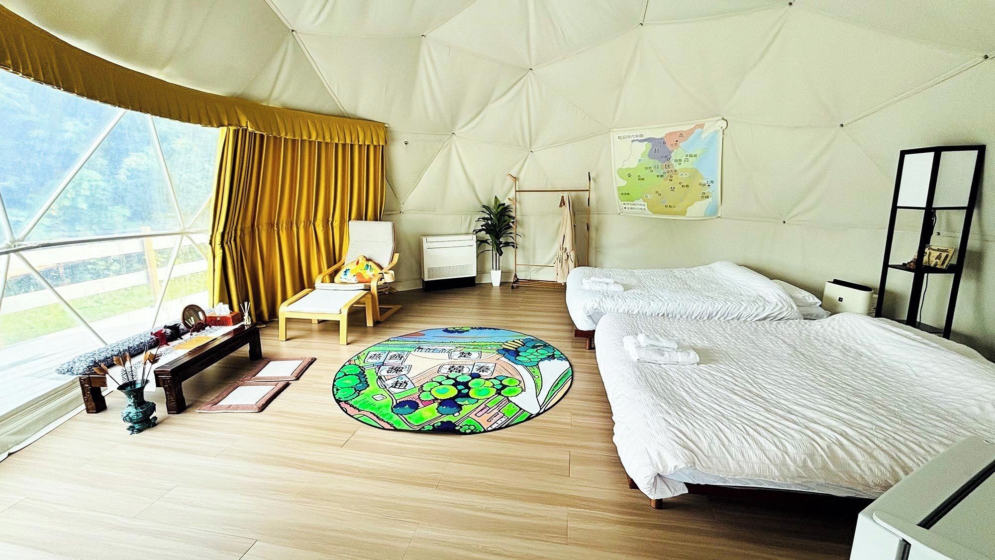 A tented room with a bed, a chair, a small table, a map on the wall, and a window with curtains.