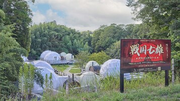 Un cartel con texto en japonés, rodeado por un paisaje natural con árboles y varias estructuras en forma de cúpula.