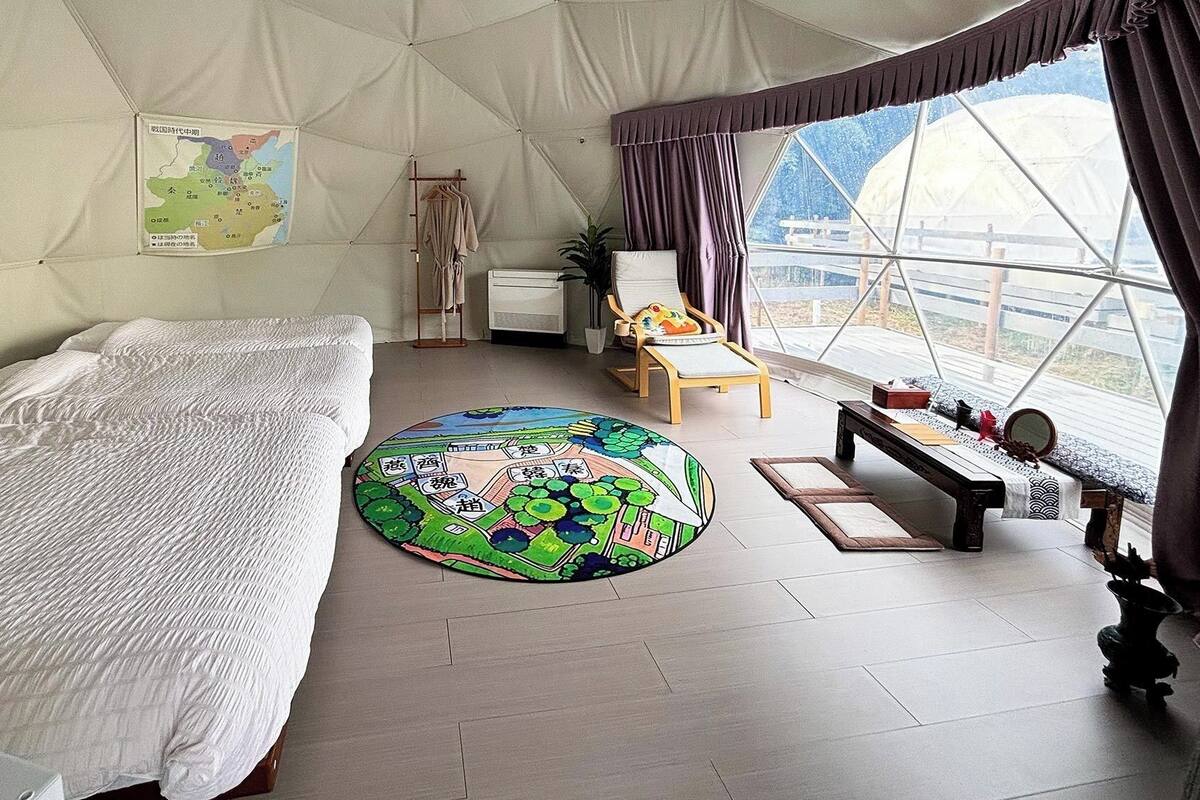 A tented room with a bed, a round rug, a chair, a table, and a map on the wall.