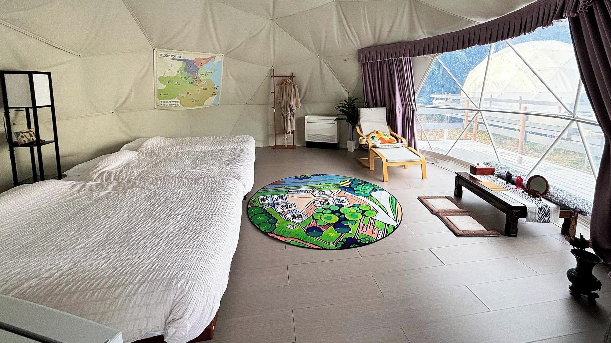 A tented room with a bed, a round rug, a chair, a table, and a map on the wall.