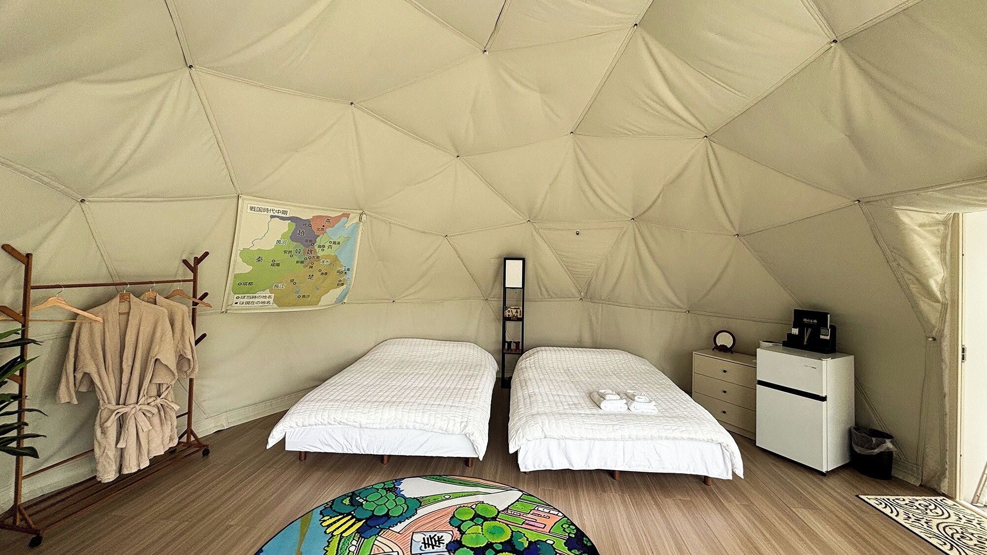 A tented room with two beds, a map on the wall, a small shelf, and a desk with a coffee machine.
