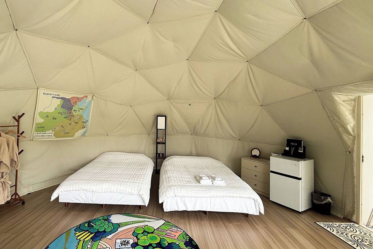 A tented room with two beds, a map on the wall, a small shelf, and a desk with a coffee machine.