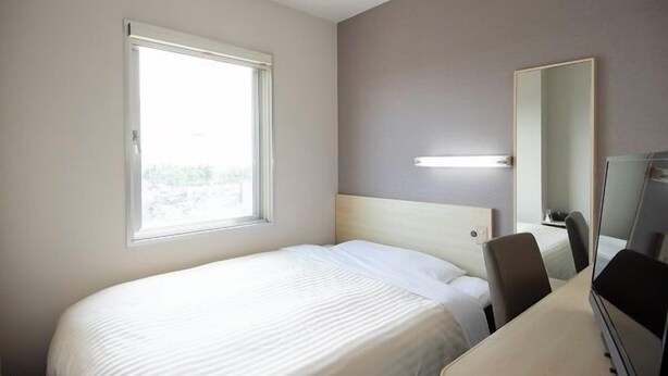 A hotel room with a bed, a desk, a chair, a mirror, and a window. - Hotel Park Inn Takaoka (Takaoka)