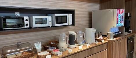 Un espace buffet proposant divers plats et équipé d’appareils tels que des micro-ondes et une machine à café.