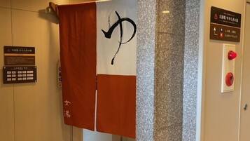 Een hotelkamer met een handdoek aan een rek, een bord met Japanse tekst en een rookmelder aan de muur.