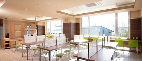 Une salle de classe moderne, dotée de tables et de chaises, de grandes fenêtres et offrant une vue sur les bâtiments environnants.