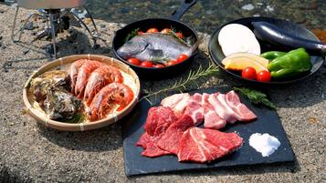 A variety of seafood and meats on a stone surface, including shrimp, fish, and steak, with cooking utensils nearby.