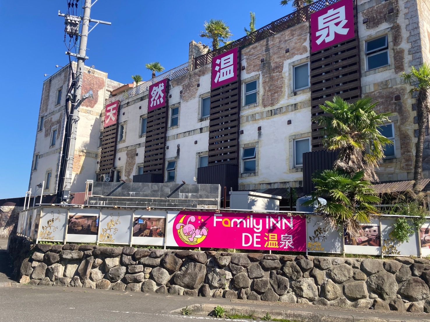 A building with multiple stories, featuring a stone wall in front and a sign for Family Inn DE 温家.