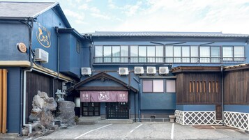 Un edificio japonés tradicional con fachada azul, varias unidades de aire acondicionado y una estructura de piedra al frente.