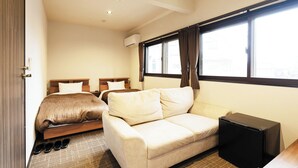 A hotel room with two beds, a sofa, a small table, a TV, and a window with curtains. - Business Hotel Hinokiya (Hitoyoshi)