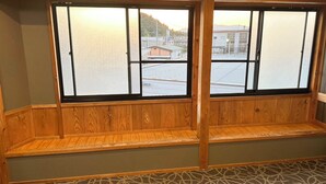 A room with a wooden bench and a large window with a view of buildings and a hill. - Business Hotel Hinokiya (Hitoyoshi)