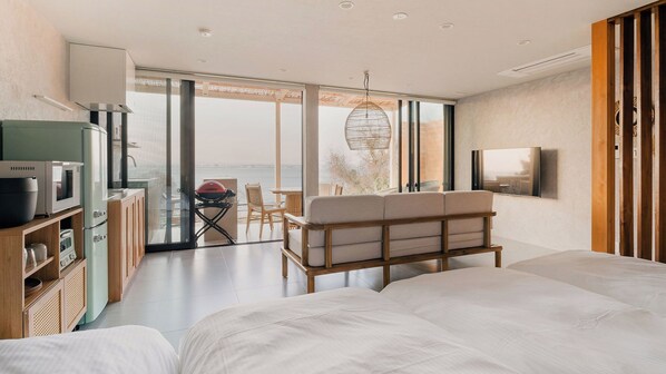 A modern bedroom with a large bed, a sofa, a TV, and a kitchenette. - Okutass Resort Villa Bali (Awaji)
