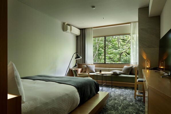 Quarto de hotel com uma cama, um sofá, uma escrivaninha, um abajur e uma televisão.