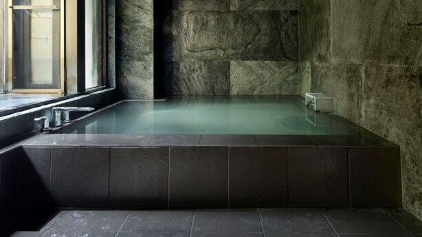 A modern spa room with a stone wall, a large window, and a bathtub. - Note/nasu (Nasu)