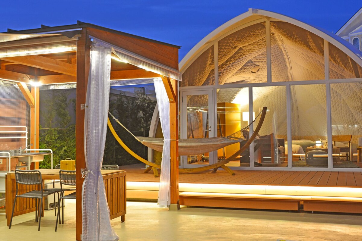 Una tienda en forma de cúpula con una terraza de madera, una hamaca y una mesa con sillas.