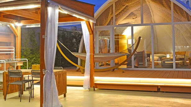 Une tente en forme de dôme dotée d’une terrasse en bois, d’un hamac et d’une table avec des chaises.