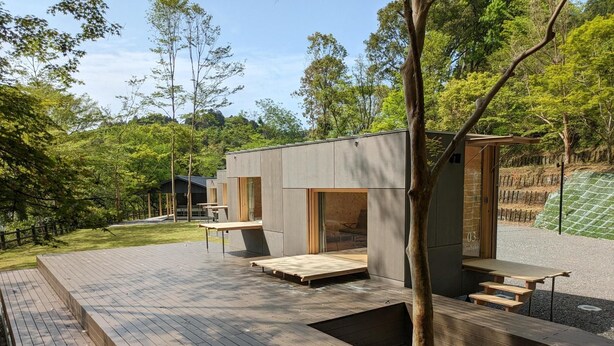 A modern outdoor area with wooden decks and built-in seating, surrounded by trees and greenery. - Snow Peak Miyakonojo Campfield (Miyakonojo)