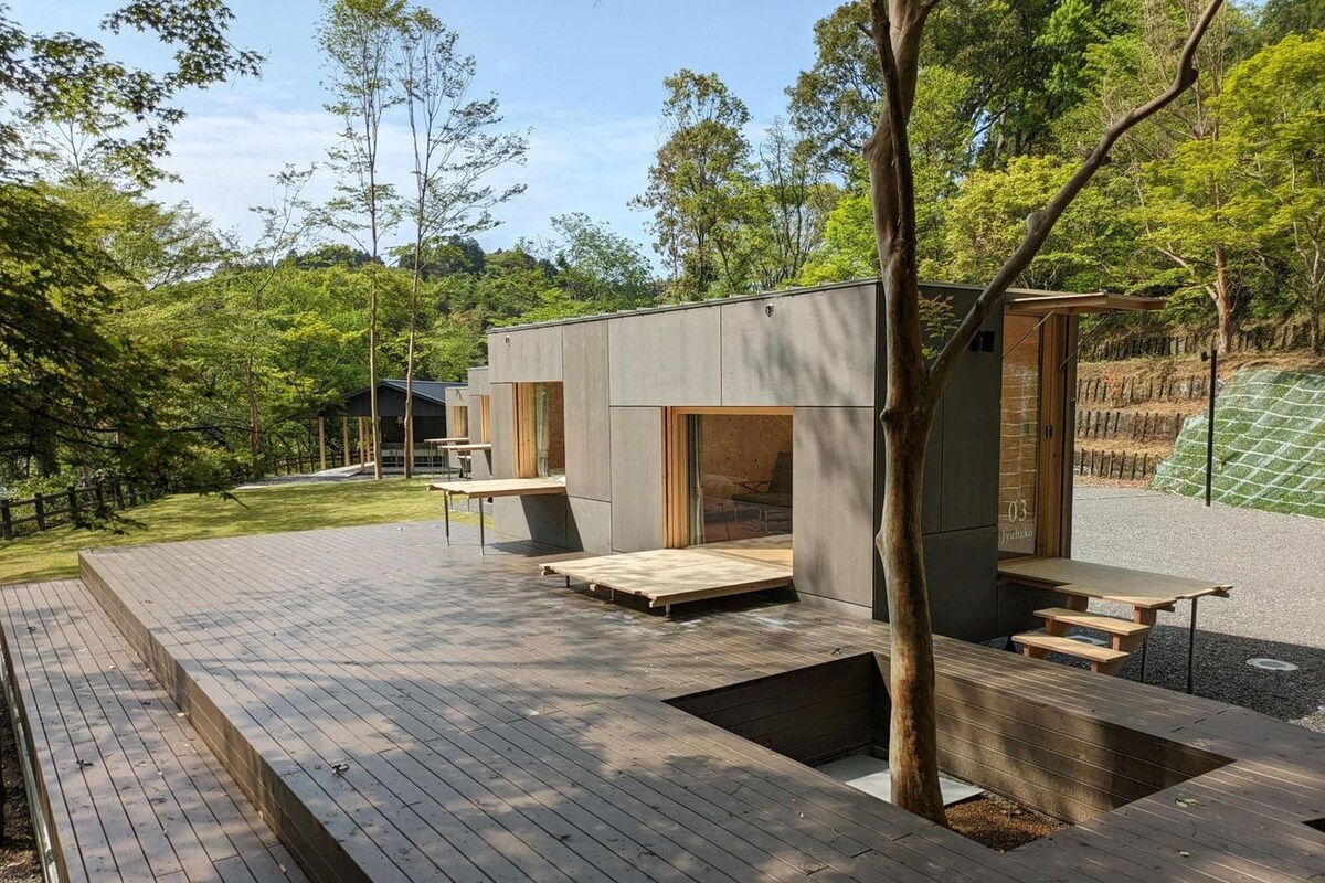 Un espacio exterior moderno con una terraza de madera, un edificio pequeño con ventanas amplias y un árbol.
