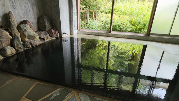 A large, reflective water feature with rocks and a view of greenery through a window. - Dai Onsen Ryokan Kanegaya (Hanamaki)