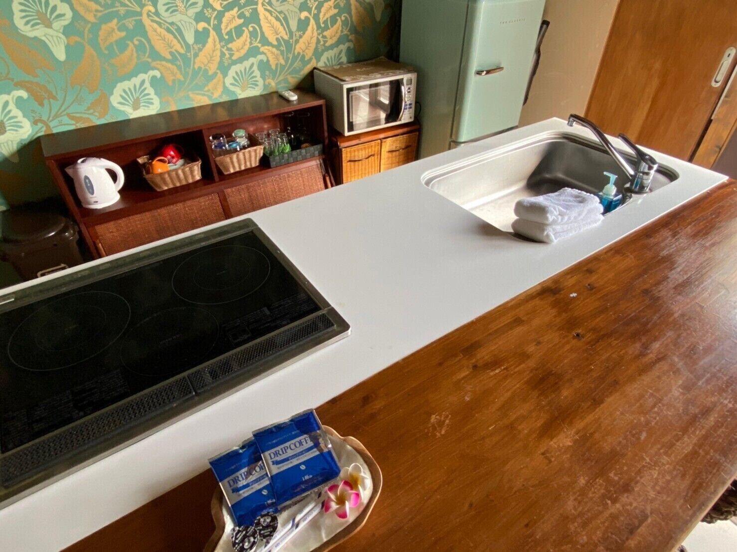 A kitchen with a microwave, a toaster, and a sink. There is a wooden cabinet with various items and a white countertop.