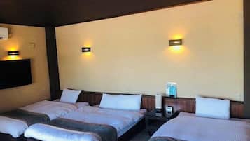 A hotel room with three beds arranged in a row, a flat-screen TV mounted on the wall, and two wall-mounted lamps.