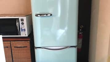 A light blue refrigerator in a kitchen with a microwave on top and a fire extinguisher in the background.